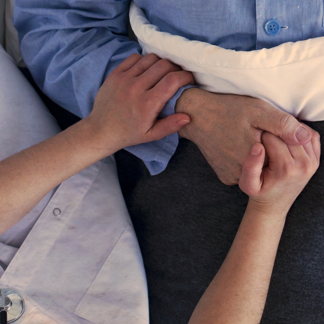 gentlemen laying down and a nurse comforting him by holding his hand